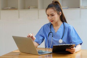 An Asian female doctor uses a laptop, to check medical records, and work in the office.