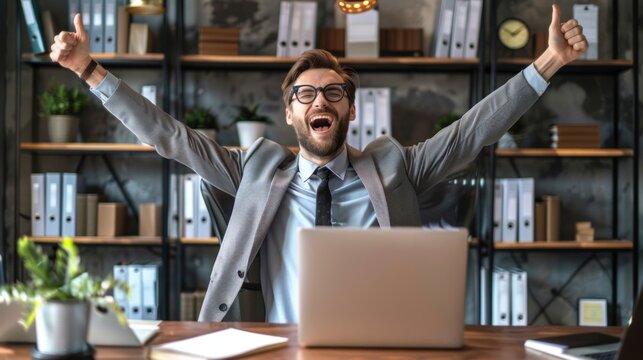 Happy businessman with arms raised shouting sitting at desk in office