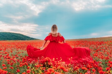 Happy woman in a long red dress in a beautiful large poppy field. Woman stands with her back in a...