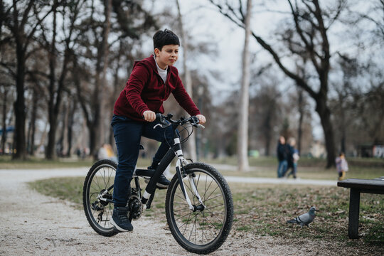 A youthful boy is captured riding his bicycle through a city park, a picture of healthy outdoor activity and carefree childhood joy.