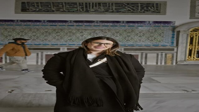 Smiling woman with glasses standing inside istanbul's historical topkapi palace, decorated with islamic calligraphy.