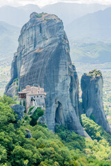 An isolated monastery atop a vertical rock formation surrounded by greenery in Meteora Greece