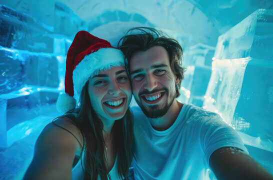 Photo of a happy couple taking a selfie with the front camera, wearing white t-shirts and Christmas hats inside an ice house with blue decorations