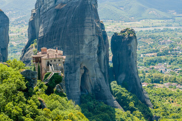 Isolated monastery sitting atop narrow rock pillars surrounded by verdant foliage in Meteora Greece