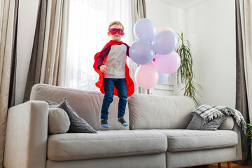 Child in superhero costume with balloons.