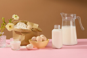Fototapeta na wymiar Brown background against cooking concept with milk, eggs and different ingredients decorated by a vase of flower on pink table. Blank space for texting or presenting product