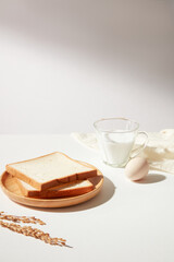 Slices of sandwich are put on a round wooden dish decorated by a cup of fresh milk, an egg, white towel and a branch of wheat. Copy space for adding text