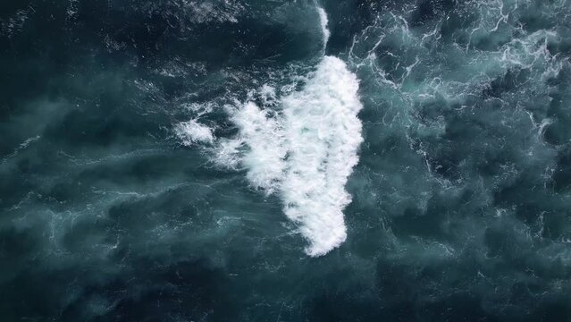 Short wave turns into white foam, moves quickly and expands, leaving behind triangular trail. Aerial view of ocean surf in a shallow location, beautiful shades of seawater