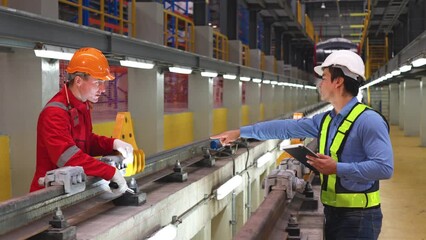 Side view professional engineer hold tablet and point to technician worker near railroad tracks of electrical or sky train in factory workplace for maintenance the track.
