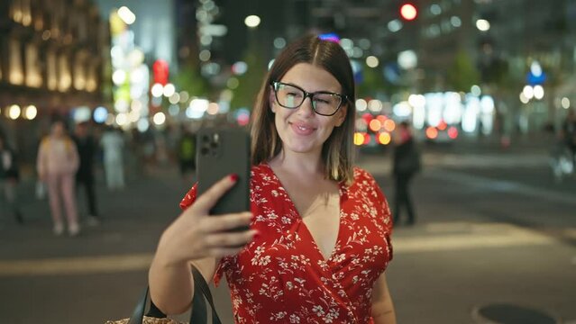 Cheerful and beautiful hispanic woman, captured in a joyful moment, texting on her smartphone under the night lights of urban osaka street, embodying the essence of a connected digital world.