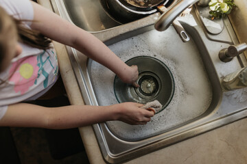 Above shot of young girl washing dishes in kitchen sink