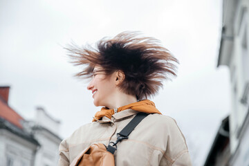 oyful Young Woman with Windswept Hair Smiling Outdoors - obrazy, fototapety, plakaty
