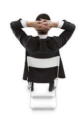 A businessman in a black suit is sitting in a chair, relaxing, with his hands behind his head on a white background, conveying a sense of ease