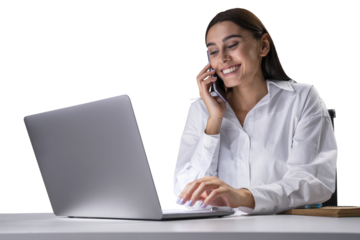 A smiling woman multitasking with a phone and laptop on a desk against a white background, depicting business communication