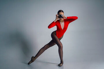 portrait of a young ballerina in a red bodysuit and pointe shoes posing with a camera in a photo studio