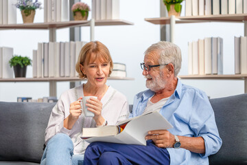 Senior couple spending time together in the living room, woman and man reading a book and enjoying coffee on the cozy sofa at home