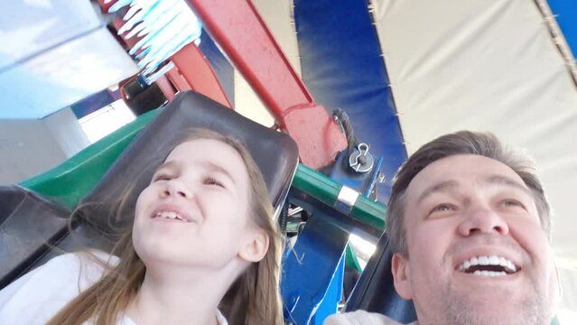 Dad and daughter go on thrill rides in an amusement park. 