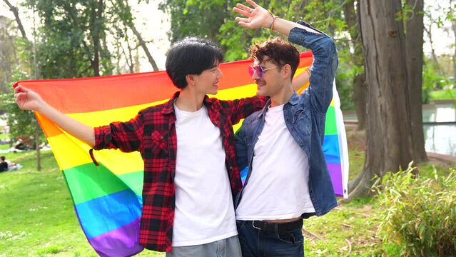Happy multi-ethnic gay couple celebrating love waving lgbt flag in a park