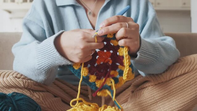 Young woman knitting crocheting with colored yarn granny square at home. Woman doing needlework, home hobbies