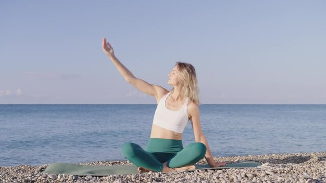 Young woman is doing yoga on the beach near the sea. A girl t does yoga exercises, and against the backdrop of the sea surf and a beautiful sky