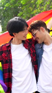 Low angle view portrait of a gay male friends raising lgbt rainbow flag in a park