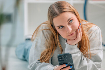 blonde girl at home with mobile phone and doubtful or thoughtful expression