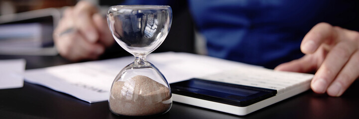 Hourglass On Desk. Running Late With Invoice