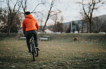 Back view of a young man enjoying a solo bicycle ride in a serene park setting with autumn foliage.