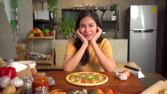 Happy cheerful Asian beautiful woman making and baking a pizza at home. 