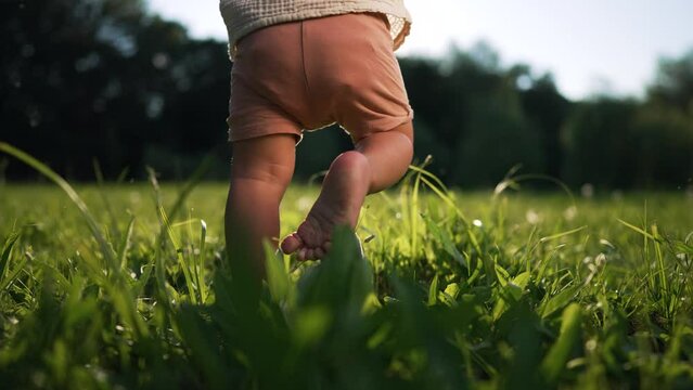 First steps. Father's Day.father helps his baby son take his first steps on grass in tpark at sunset. Happy family concept.Dad and son outdoors in summer.Father teaches his son to take his first steps