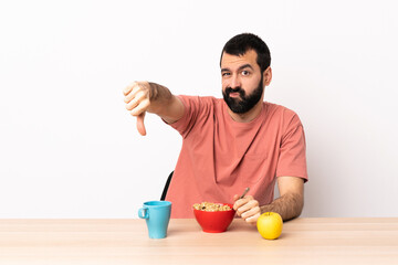 Fototapeta na wymiar Caucasian man having breakfast in a table showing thumb down with negative expression.