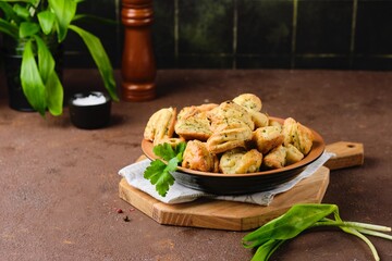 Unsweetened curd cookies with parsley and wild garlic in a ceramic plate on a brown concrete background. Baking with herbs, wild garlic recipes.