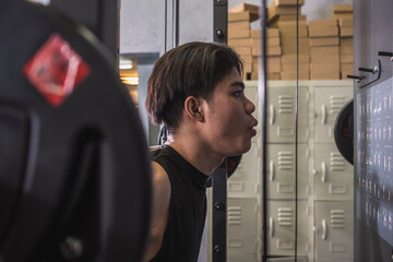 Dedicated and focused novice male does proper breathing while doing back squats on a smith machine in a well-equipped gym. A beginner starting to workout and train. - obrazy, fototapety, plakaty