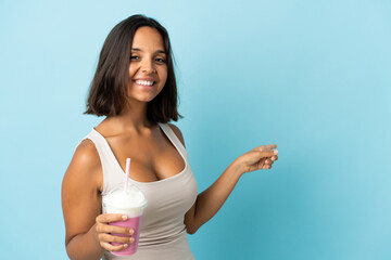 Young woman with strawberry milkshake isolated on blue background pointing back