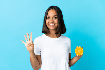 Young asian girl holding an orange isolated on blue background happy and counting four with fingers