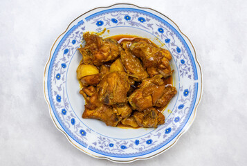 Delicious chicken bhuna curry on a plate on white background. Top view of Bengali (Bangladesh) cuisine dish with chicken meat, potato, and spicy gravy. Tasty Asian food. 