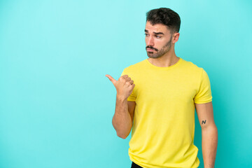 Young caucasian man isolated on blue background unhappy and pointing to the side
