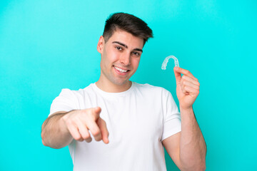 Young caucasian man wearing holding invisible braces isolated on blue background points finger at...