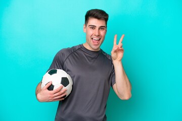 Young caucasian football player man isolated on blue background smiling and showing victory sign