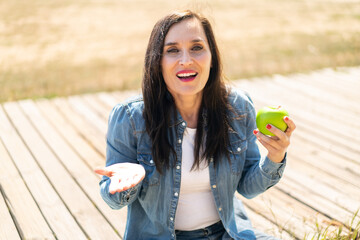 Middle aged woman with an apple at outdoors with shocked facial expression