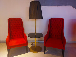 The floor lamp is located between two red sofa chairs.