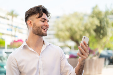 Young handsome man using mobile phone at outdoors with happy expression