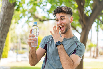 Young handsome sport man with a bottle of water at outdoors with surprise and shocked facial...