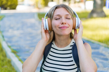 Young blonde woman at outdoors listening music