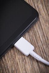 Black smartphone and connected white cable of charger. Telephone charging