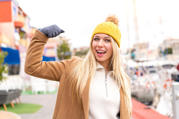 Young pretty blonde woman wearing winter jacket at outdoors doing strong gesture