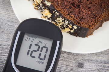 Glucometer with result sugar level and sweet chocolate cake. Nutrition during diabetes
