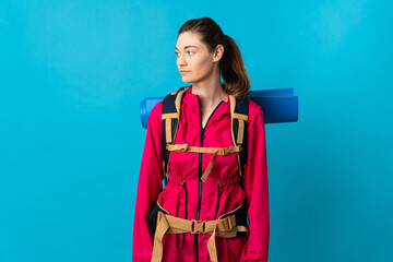 Young mountaineer woman over isolated blue background looking to the side