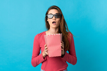 Young Ireland woman isolated on blue background surprised with 3d glasses and holding a big bucket...