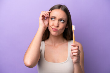 Young caucasian woman brushing teeth isolated on purple background having doubts and with confuse face expression